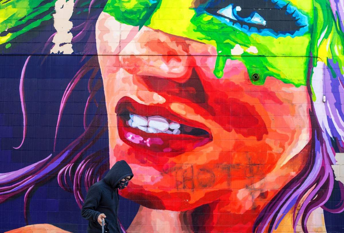 A masked pedestrian walks past a mural in Edmonton, Sunday, Dec. 20, 2020.