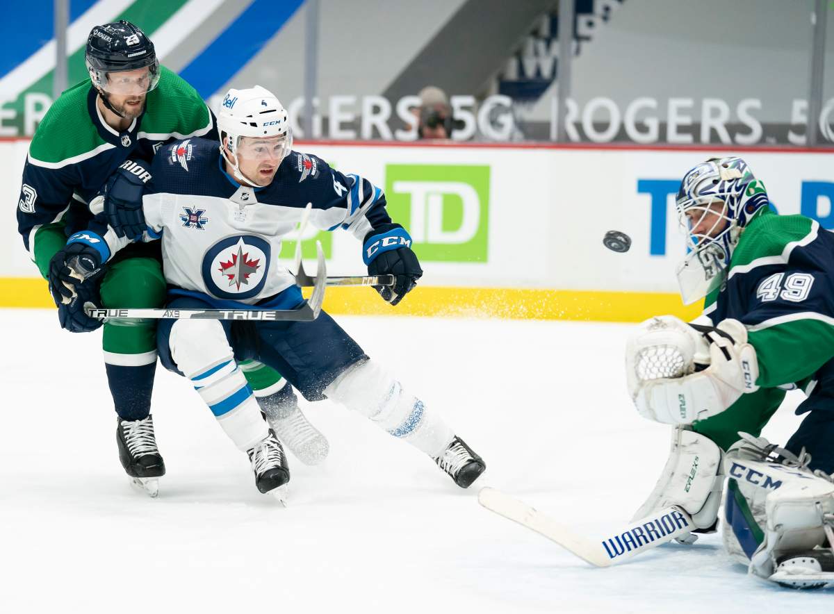 Vancouver Canucks goaltender Braden Holtby (49) stops a shot from Winnipeg Jets defenceman Neal Pionk (4) as Vancouver Canucks defenceman Alexander Edler (23) looks on during first-period NHL action in Vancouver, Sunday, Feb. 21, 2021. 