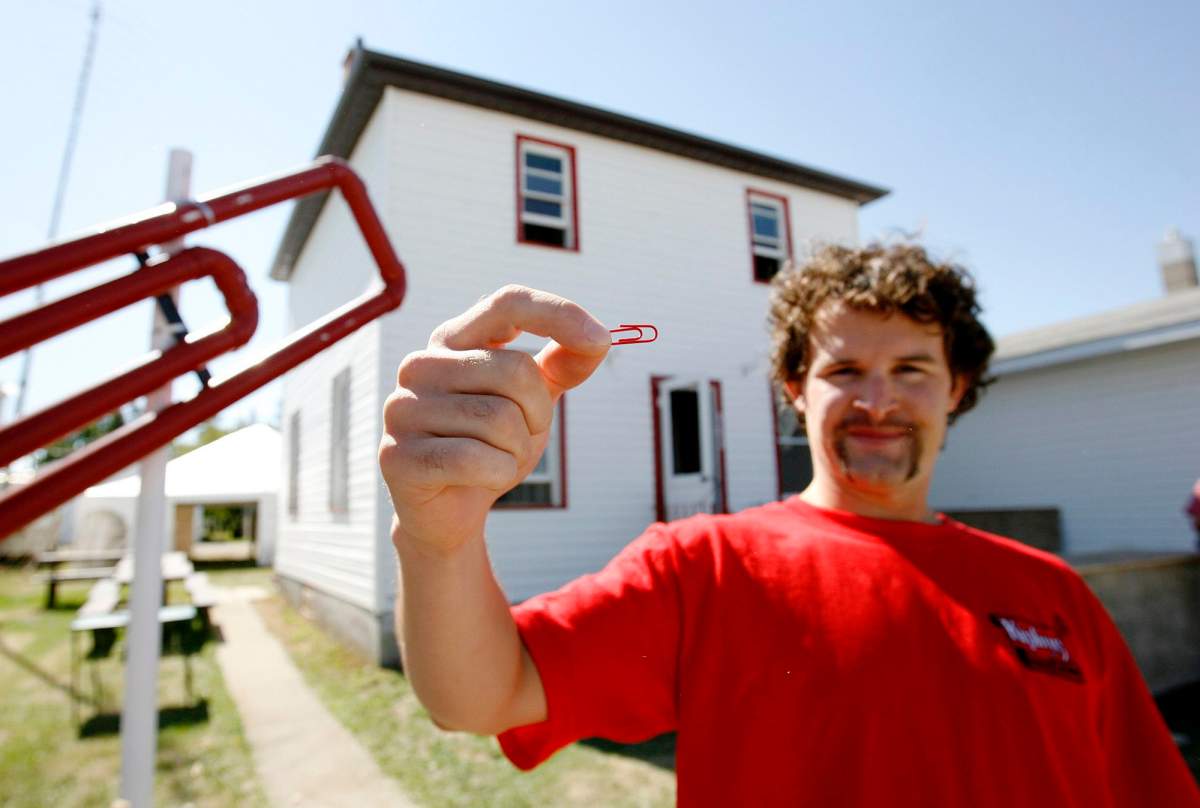 Kyle MacDonald holds up a red paper clip in front of his house in Kipling, Sask. on Friday, Sept. 1, 2006. The small Saskatchewan farming town is rolling out the red carpet for a weekend-long house-warming party for Kyle MacDonald, who traded up from a red paper clip all the way up to a house. (CP PHOTO/Troy Fleece)