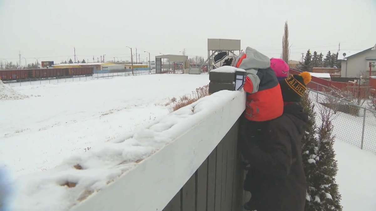 Paul Nicholson and his children peering over their backyard fence at the CN Rail Dunvegan Yard in Edmonton, Alta., on Friday, Feb. 5, 2021.