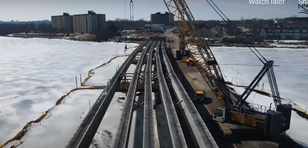 Some of the massive concrete girders are laid out in preparation for bridge decking, alongside a temporary causeway to support cranes and other construction equipment.