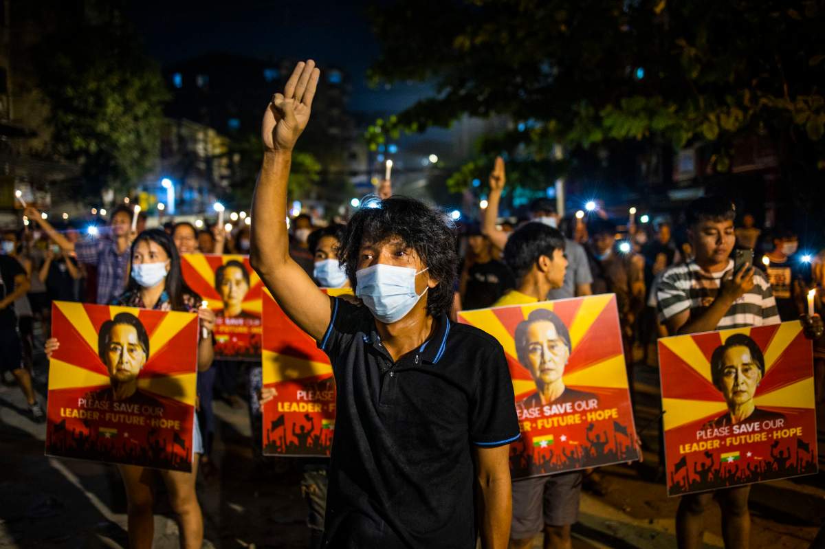 A man flashes the three-fingered gesture while others hold images of deposed Myanmar leader Aung San Suu Kyi during a candlelight night demonstration held out on the street despite a curfew imposed by authorities in Yangon, Myanmar on March 12, 2021.