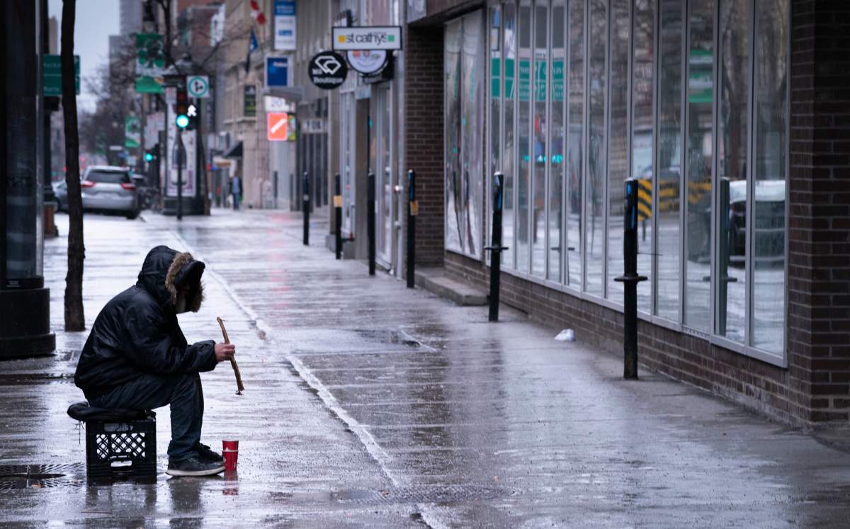 A homeless person sits alone on a sidewalk in downtown Montreal on Monday, March 30, 2020.
