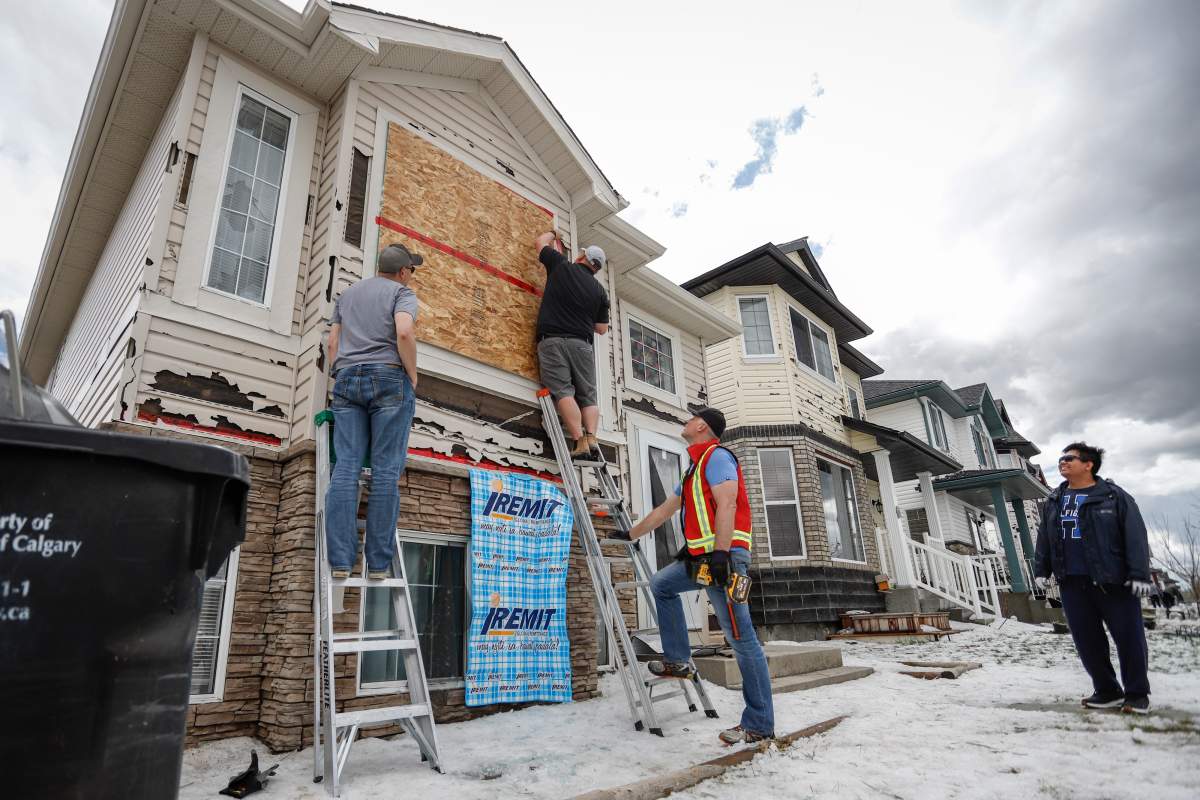 Meynard David, right, looks on as volunteers help board up his house as residents begin cleaning up in Calgary, Alta., Sunday, June 14, 2020, after a major hail storm-damaged homes and flooded streets on Saturday.