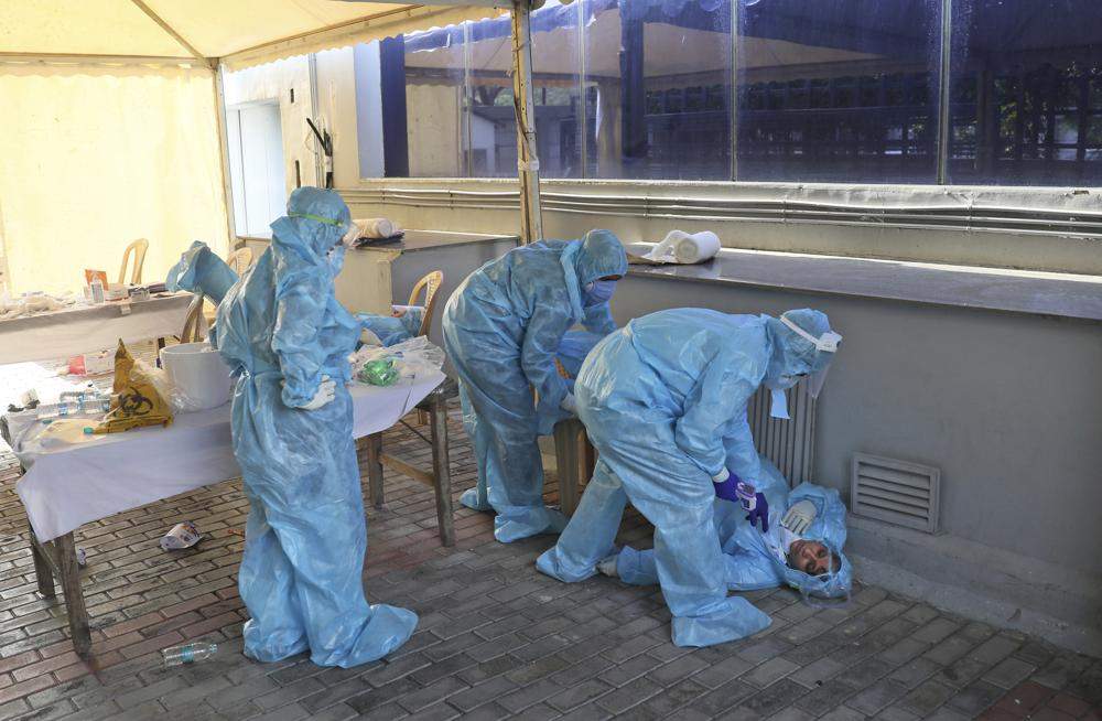 In this April 27, 2020, file photo, health workers attend to a colleague who fainted due to exhaustion and long working hours at a COVID-19 testing center in New Delhi, India.