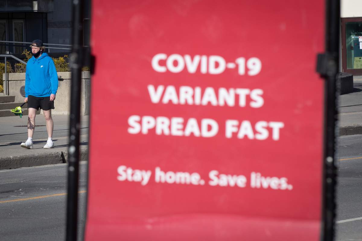 A person wears a mask to protect them from the COVID-19 virus while walking by information about the ongoing pandemic in Kingston, Ontario on Monday, April 5, 2021. THE CANADIAN PRESS IMAGES/Lars Hagberg.