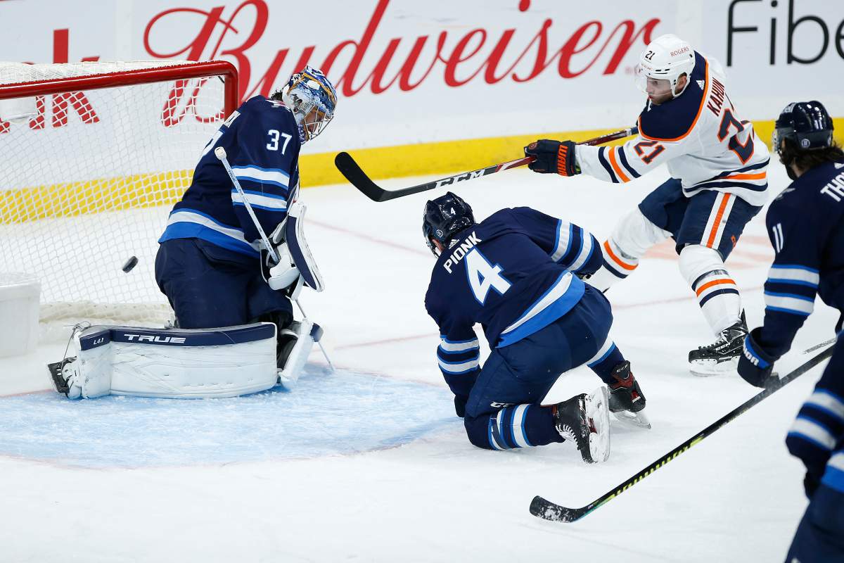 Winnipeg Jets goaltender Connor Hellebuyck (37) saves the shot from Edmonton Oilers' Dominik Kahun (21) as Neal Pionk (4) defends during second period NHL action in Winnipeg on Saturday, April 17, 2021. 