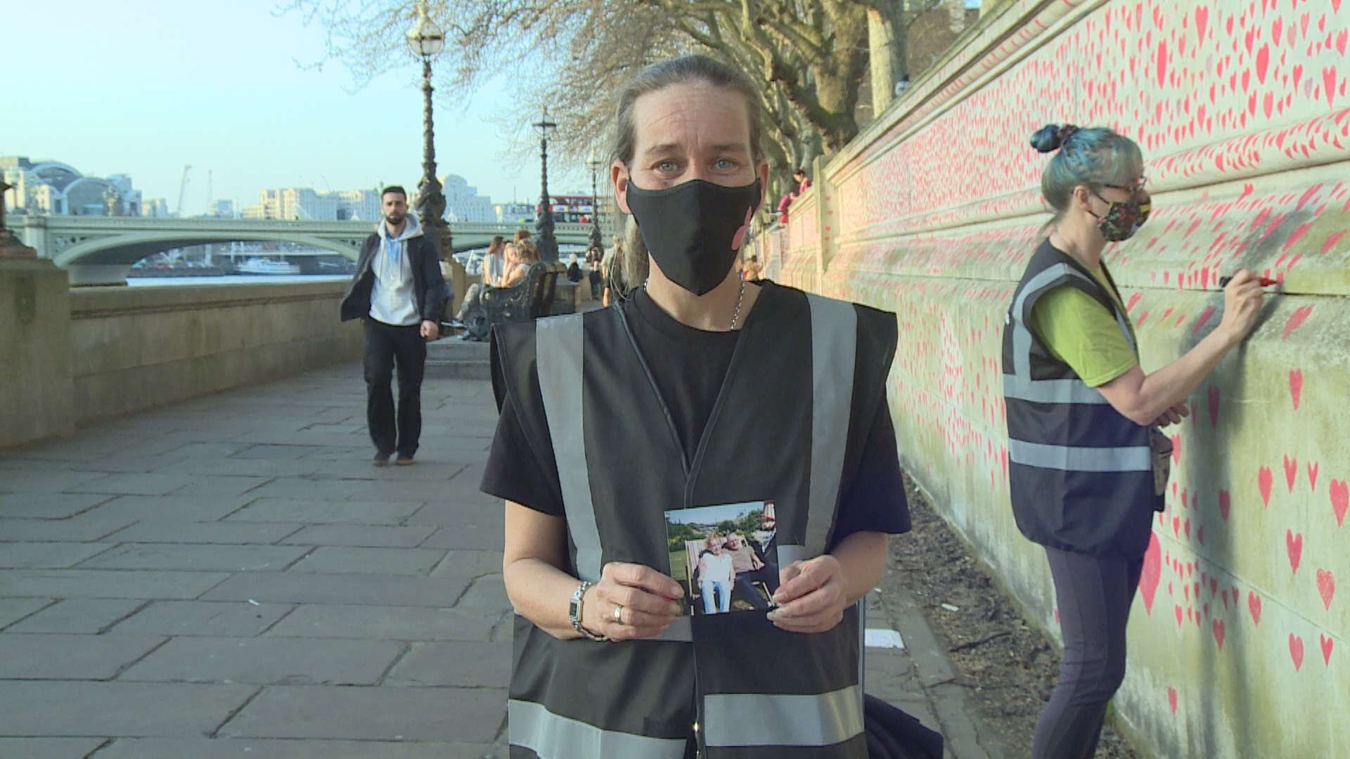 Sophie Rawlings stands at the National COVID Memorial Wall in London, England, holding a picture of her parents Brian and Pauline, who died within seven days of each other after contracting COVID-19.