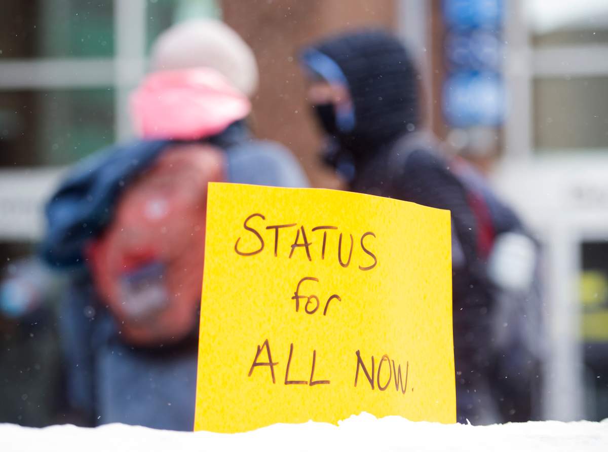 A sign reading "Status for All Now" is shown planted in a snowbank during a protest in Montreal, Saturday, January 30, 2021, to demand status for all workers and to demand dignity for all non status migrants as full human beings as the COVID-19 pandemic continues in Canada and around the world. THE CANADIAN PRESS/Graham Hughes.
