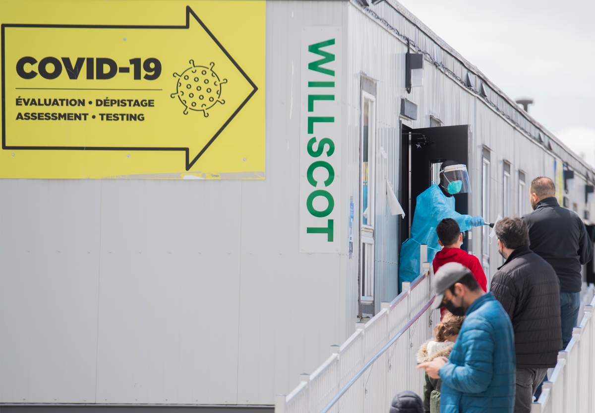 A health-care worker hands a face mask to people waiting to enter a COVID-19 testing clinic in Montreal, Sunday, May 9, 2021, as the COVID-19 pandemic continues in Canada and around the world. 