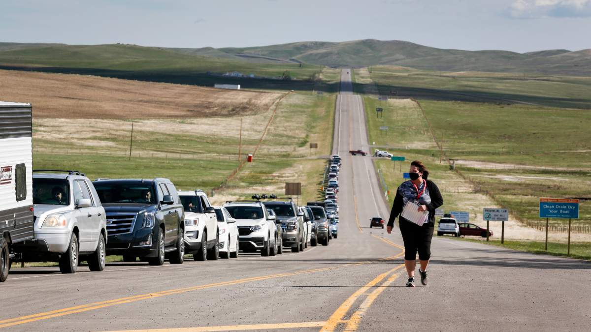 Catherine Bechard, a CBSA regional Indigenous Affairs advisor, walks along a line-up of southern Alberta residents waiting to get shots of a COVID-19 vaccine from a Montana tribe in Carway, Alta., Tuesday, May 18, 2021.