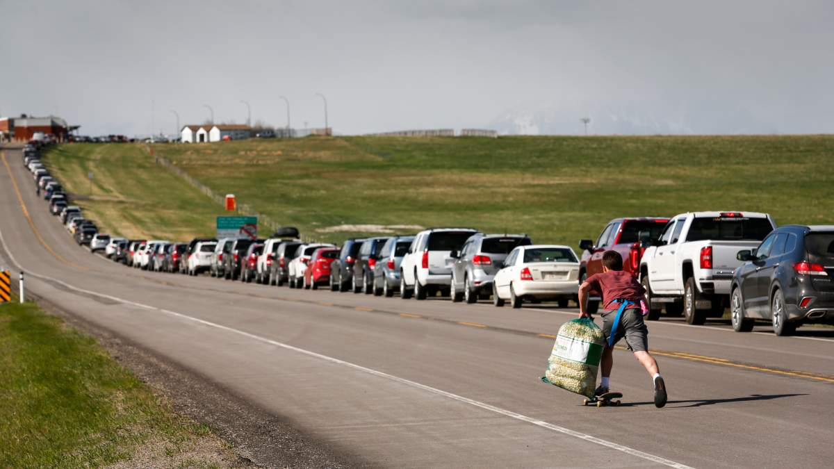 A teenaged boy uses a skateboard to move up and down selling popcorn to Southern Alberta residents lining up to get shots of a COVID-19 vaccine from a Montana tribe in Carway, Alta., Tuesday, May 18, 2021.