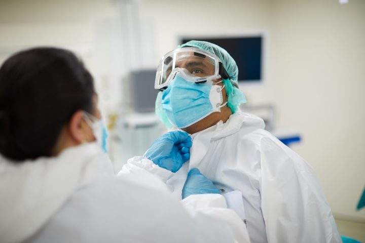 A health-care worker helps a coworker with PPE coveralls.