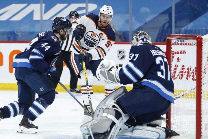 Winnipeg Jets goaltender Connor Hellebuyck (37) saves the shot from Edmonton Oilers’ Connor McDavid (97) as Jets’ Josh Morrissey (44) defends during first period NHL action in Winnipeg on Wednesday, April 28, 2021.