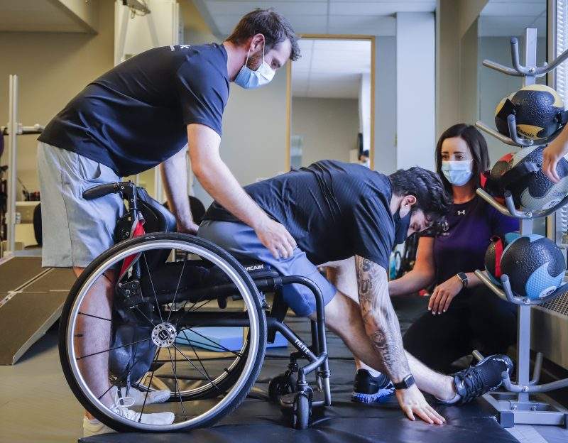 Humboldt Broncos bus crash survivor Ryan Straschnitzki, centre, is helped into his wheelchair by Eric Daigle, left, and Jill Mack while he attends a physiotherapy session in Calgary, Alta., Thursday, June 24, 2021.