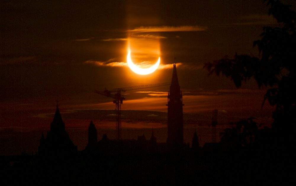 An annular solar eclipse rises over construction cranes and the Peace Tower on Parliament Hill in Ottawa on Thursday, June 10, 2021.