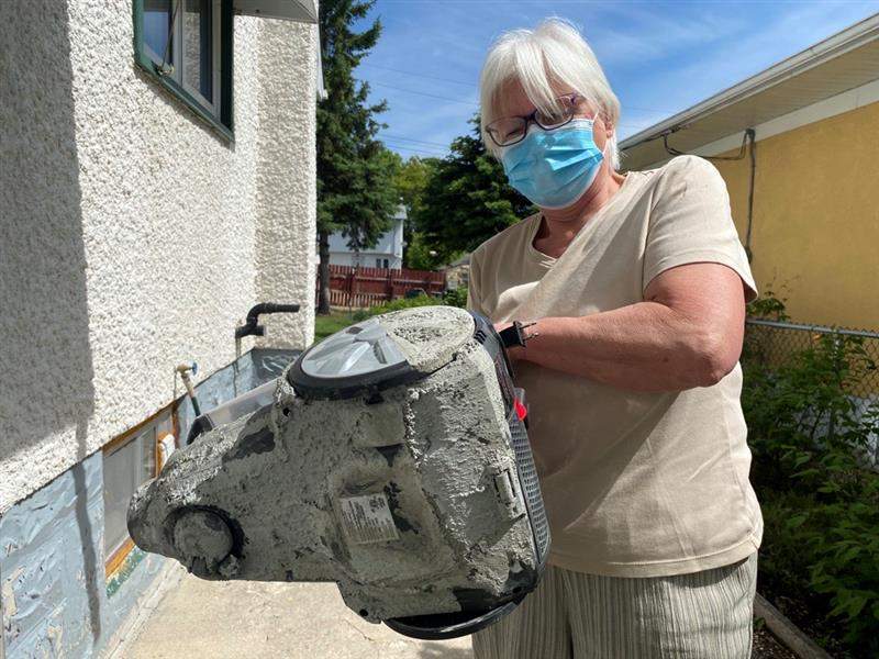 Steffie Shrimpton holds up a vacuum left coated in hardened cement when cement flooded the basement of her Semple Avenue home Saturday.