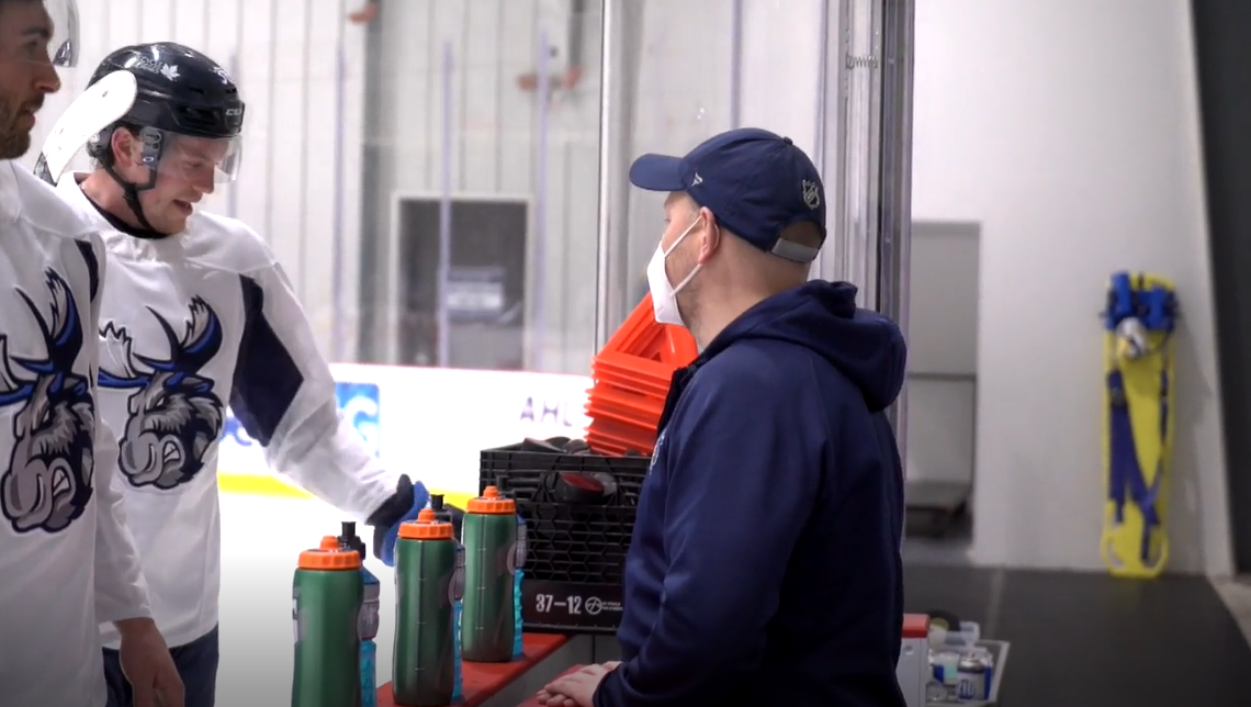 Moose head athletic therapist Zach Salmonson chats with players on the bench during a Moose practice in March 2021 at Bell MTS Iceplex.