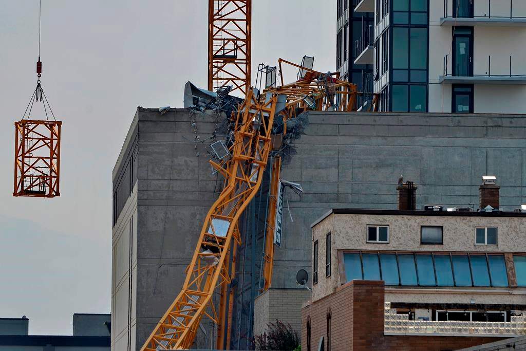 FILE. A section (left) of the vertical column of a construction crane is lowered past the mangled section of the fallen boom in Kelowna, B.C., Wednesday, July 14, 2021, following a fatal collapse of the crane.   