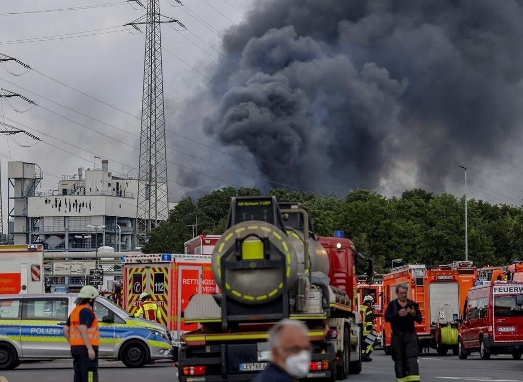 Emergency vehicles of the fire brigade, rescue services and police stand not far from an access road to the Chempark over which a dark cloud of smoke is rising in Leverkusen, Germany, Tuesday, July 27, 2021.