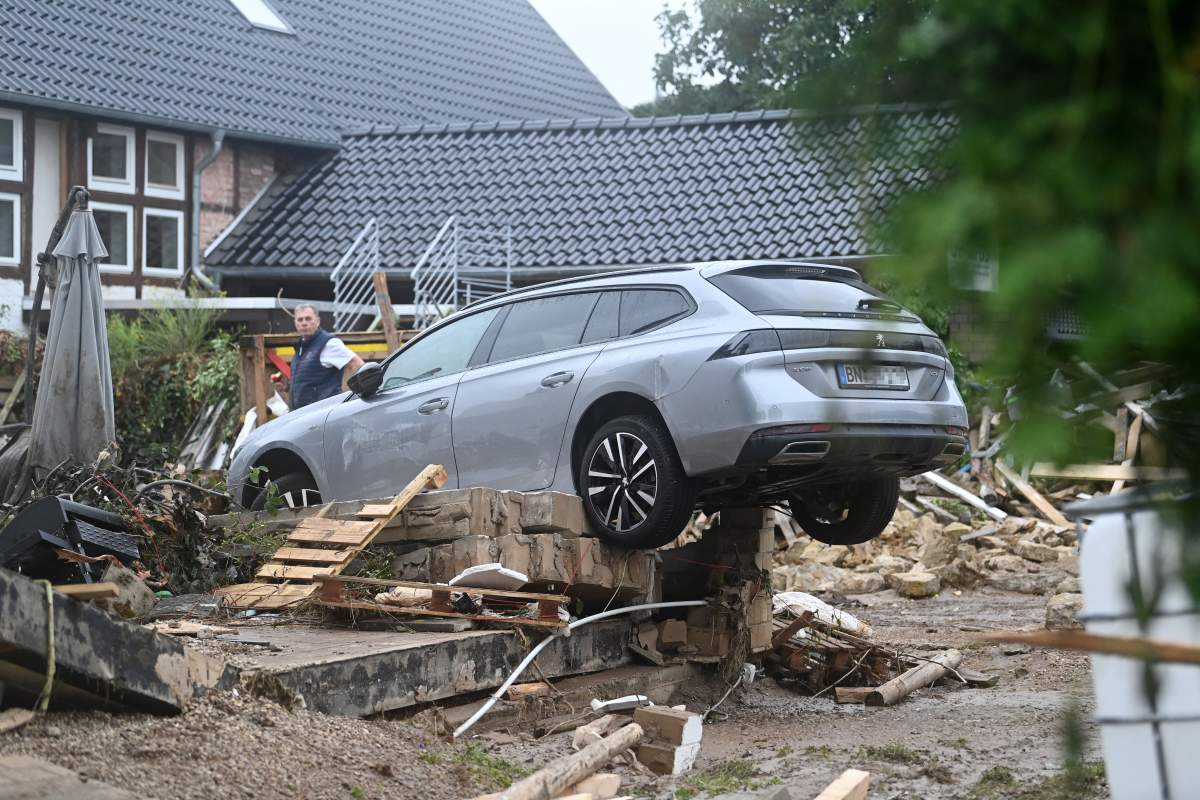 A resident stands next to debris and a damaged car in Iversheim, near Bad Muenstereifel, western Germany, on July 16, 2021, following heavy rains and floods.