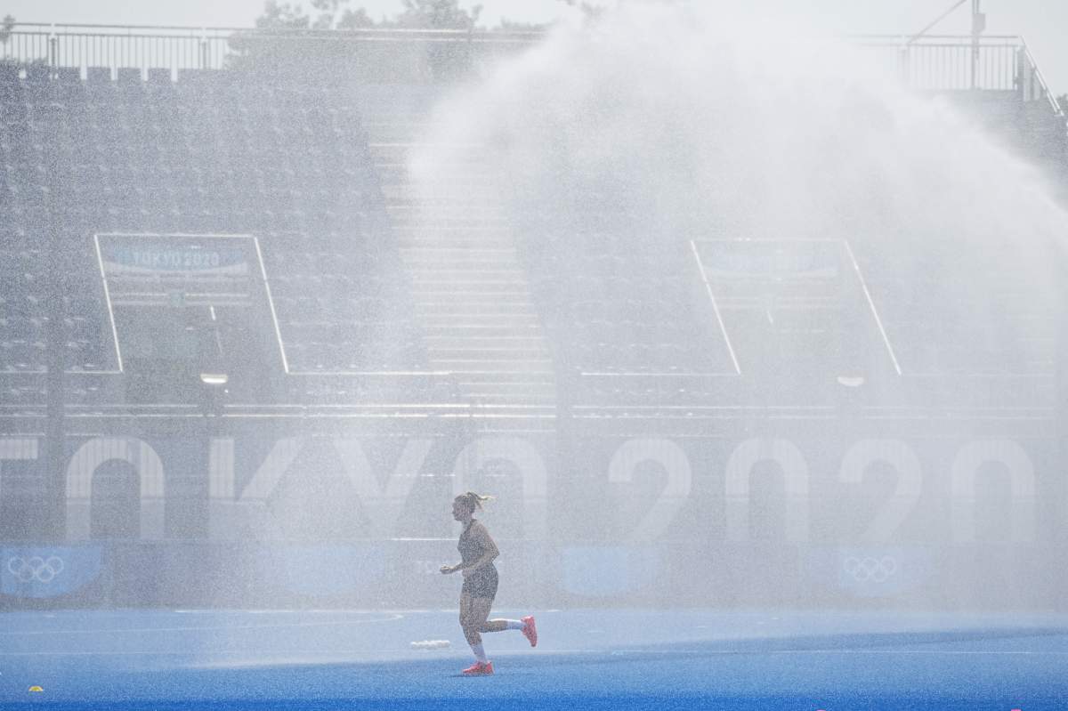 A German field hockey player runs through the sprinkling rain of the watering system before the start of a game on July 20, 2021. In the morning it was already around 30 degrees.