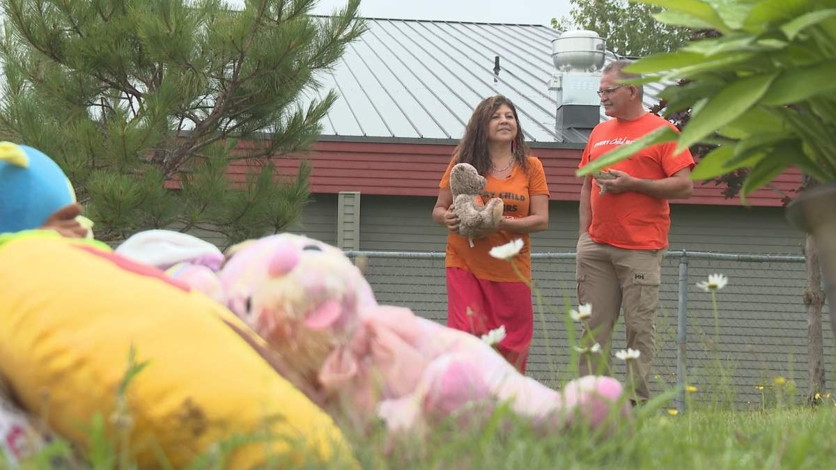 Victoria Ginnish and her husband Stephen stand near a collection of teddy bears and pairs of shoes were laid in response to the discovery of hundreds of unmarked graves at former residential schools.