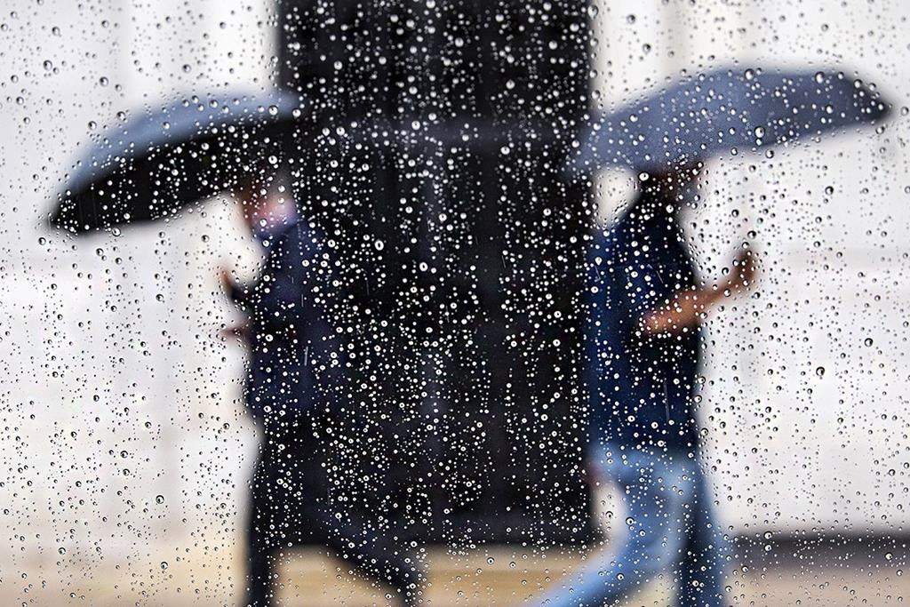 Raindrops form on a window as pedestrians shield from the rain with umbrellas in this file photo.