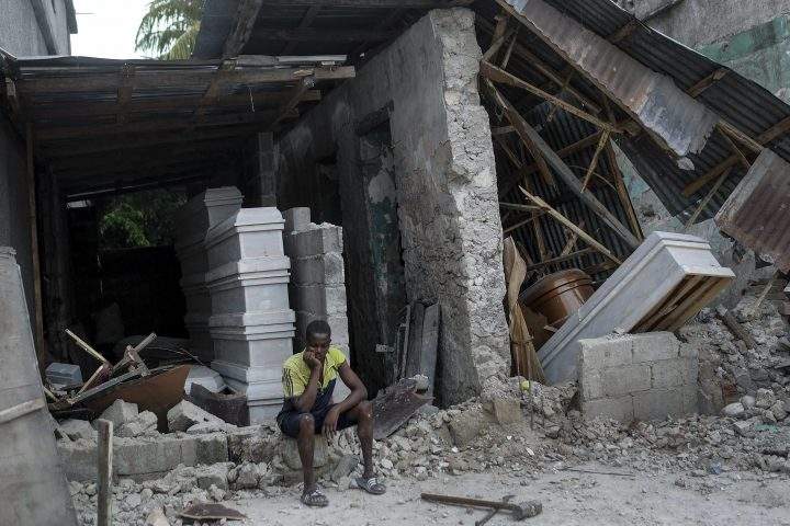 A man sits in front of a collapsed funeral home in Les Cayes, Haiti, Monday, Aug. 16, 2021