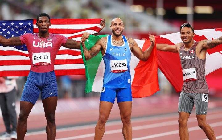 Bronze medalist Andre De Grasse of Team Canada, gold medalist Lamont Marcell Jacobs of Team Italy and silver medalist Fred Kerley of Team United States pose on the track following the Men’s 100m Final