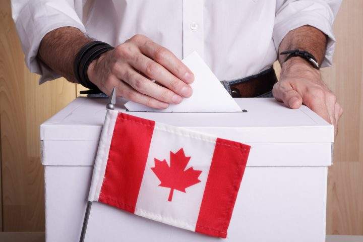 A man casting his vote. The Canadian flag is in front of the ballot box.
