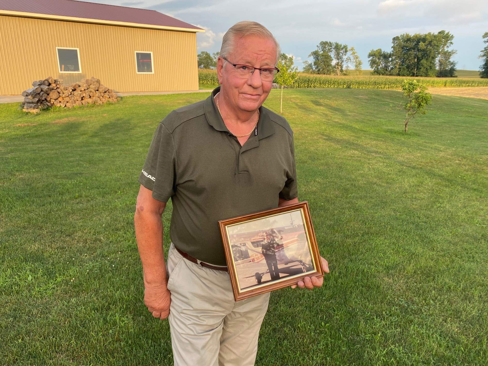 Man holding framed photo of self beside small airplane