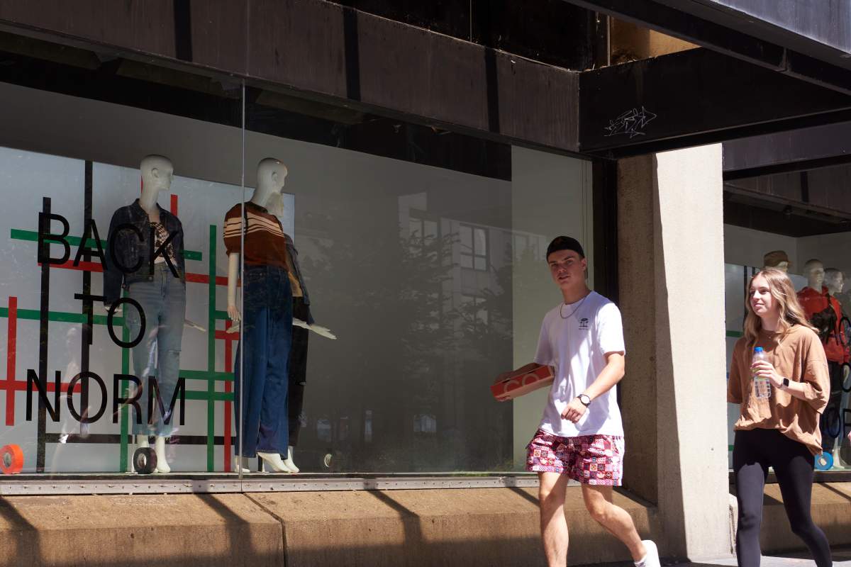 Young adults carrying takeout food walk past a 'BACK TO NORM' Hudson’s Bay window display on Bloor Street in Toronto on Aug. 15, 2021, as Ontario enters a fourth wave of the COVID-19 pandemic. 