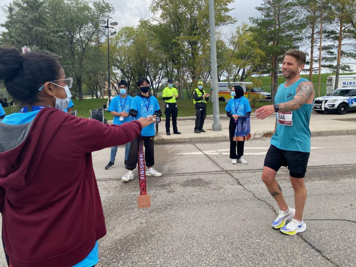 A Manitoba Marathon participant accepts his finishing medal at the first in-person race in over two years.