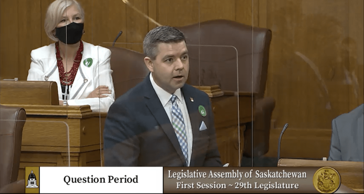 MLA Nadine Wilson shown behind MLA Jeremy Harrison wearing a ‘Stick it to COVID’ sticker.