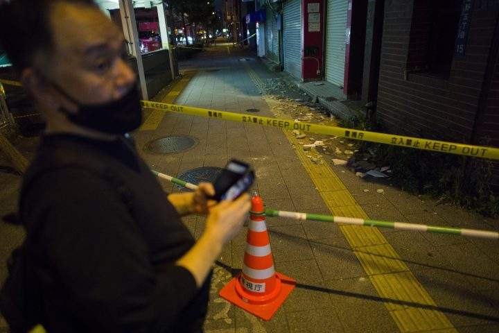 A pedestrian checks out a cordoned-off area covered in debris after part of the building wall fell in Tokyo early Friday, Oct. 8, 2021, following an earthquake late Thursday. 