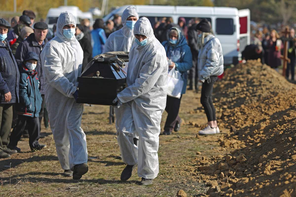 Cemetery workers in protective gear bury people who died of causes related to COVID-19 at the Novo-Yuzhnoye Cemetery in Omsk, Russia on Oct. 9, 2021.