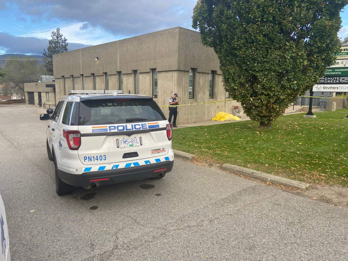 A Penticton RCMP officer takes notes while standing next to a yellow tarp at 1101 Main St. in Penticton, B.C., on Sunday, Oct. 3, 2021. 