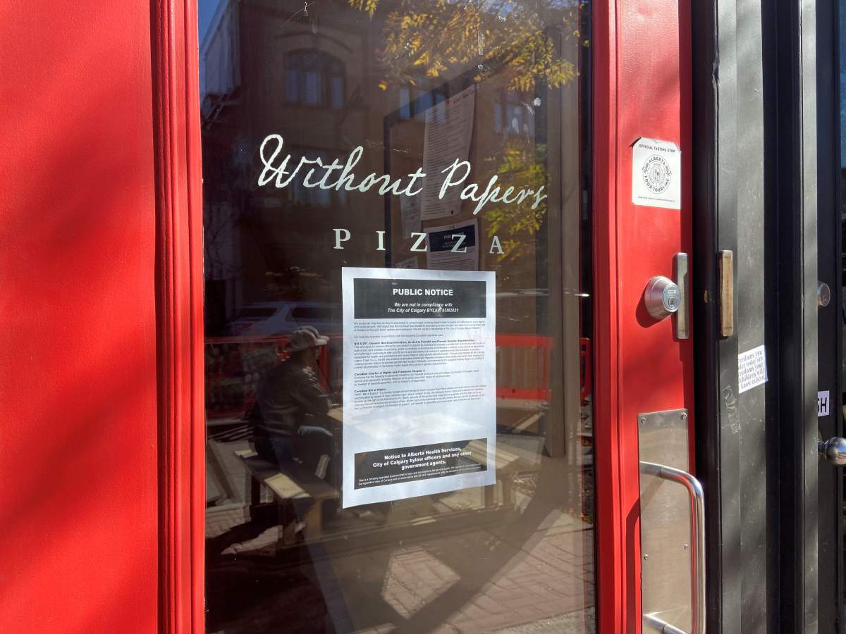 A sign at Without Papers Pizza in Inglewood states: "We are not in compliance with the City of Calgary bylaw 65M2021.".