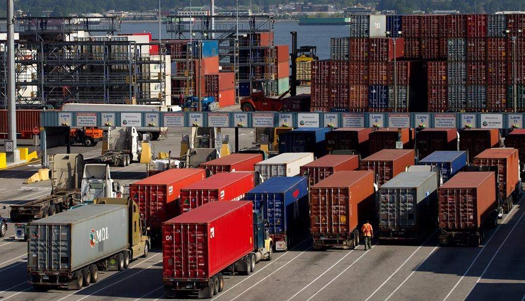 A man walks between transport trucks waiting to deliver cargo containers at Port Metro Vancouver's Center container facility in Vancouver, B.C., on Friday May 10, 2013. THE CANADIAN PRESS/Darryl Dyck.