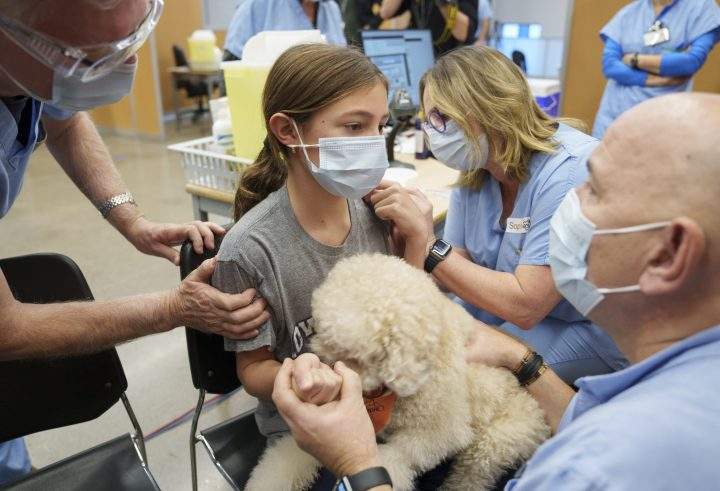 Mika-Ella Varin, 11, holds Bemol as she gets vaccinated during the first day of vaccination for children aged five- to 11-years old in Montreal, Wednesday, Nov. 24, 2021. A health care worker brought his dog Bemol to distract children during vaccination. THE CANADIAN PRESS/Paul Chiasson