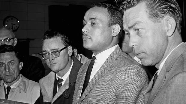 Khalil Islam, center, is booked as the third suspect in the slaying of Malcolm X, in New York, March 3, 1965. Islam, previously known as Thomas 15X Johnson, one of two men convicted in the assassination of Malcolm X, is set to be cleared after more than half a century, with prosecutors now saying authorities withheld evidence in the civil rights leader's killing, according to a news report Wednesday, Nov. 17, 2021. Detective John Keeley is at right.