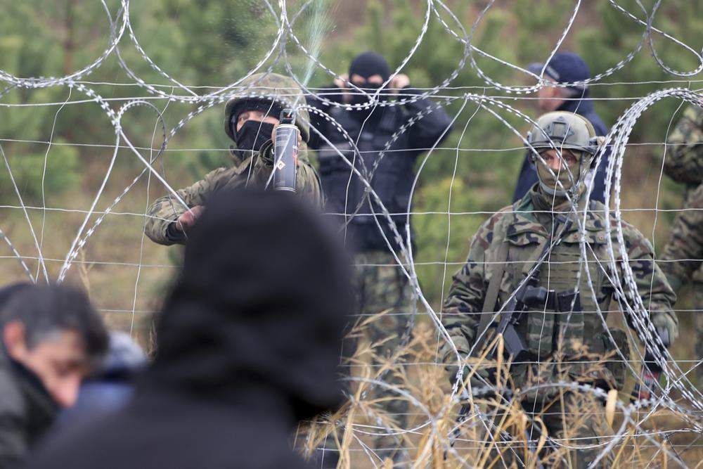 Polish border guards stand near the barbed wire as migrants from the Middle East and elsewhere gather at the Belarus-Poland border near Grodno, Belarus, Monday, Nov. 8, 2021.