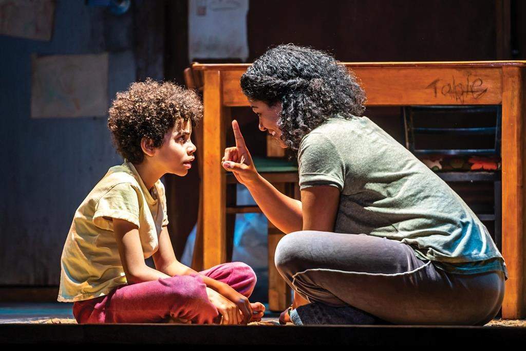 Photo of an actress and young actor sitting down on stage performing.