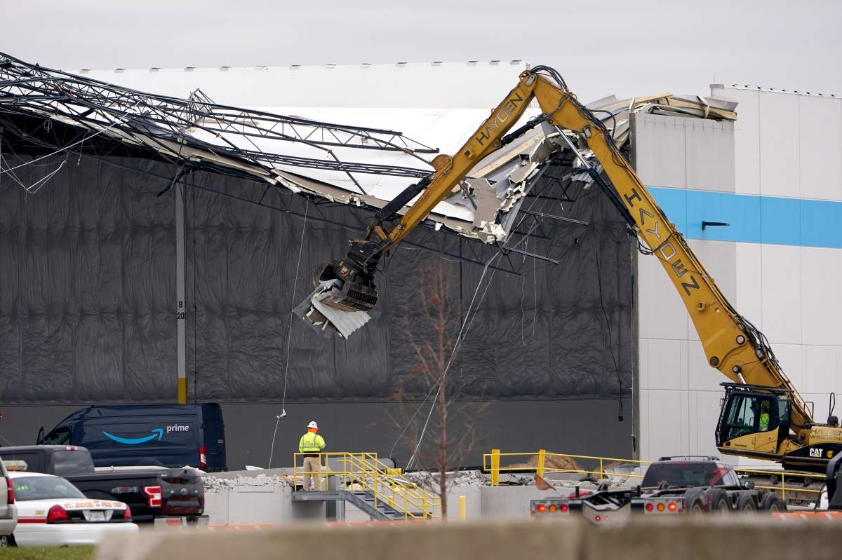 Workers use equipment to remove a section of roof left on a heavily damaged Amazon fulfillment center Saturday, Dec. 11, 2021, in Edwardsville, Ill.