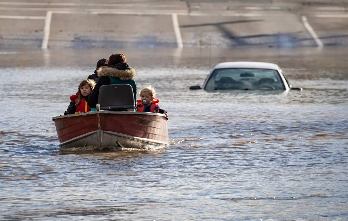 A woman and children who were stranded by high water due to flooding are rescued by a volunteer operating a boat in Abbotsford, B.C., on Tuesday, November 16, 2021.