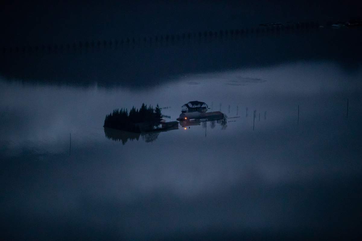 A house and a barn are surrounded by floodwaters on a farm at dusk in Abbotsford, B.C., on Monday, November 22, 2021.