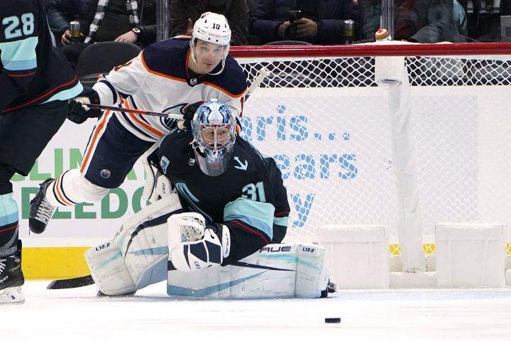 Edmonton Oilers left wing Zach Hyman, top, and Seattle Kraken goaltender Philipp Grubauer eye the puck in front of the goal during the first period of an NHL hockey game Friday, Dec. 3, 2021, in Seattle.