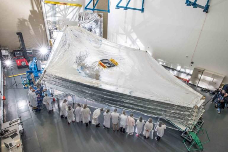 Scientists surround a full-sized replica of JWST’s five-layer sunshield, which is the largest part of the observatory