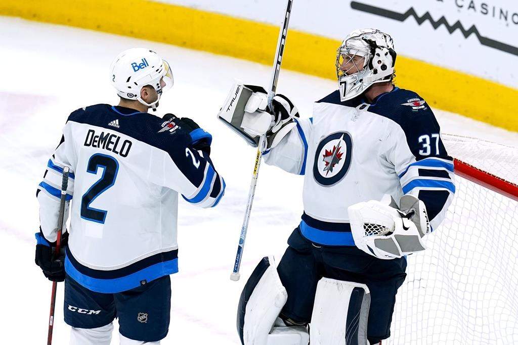 Winnipeg Jets goaltender Connor Hellebuyck (37) and defenceman Dylan DeMelo (2) celebrate at the end of the team’s NHL hockey game against the Arizona Coyotes on Tuesday, Jan. 4, 2022, in Glendale, Ariz. The Jets won 3-1. (AP Photo/Ross D. Franklin)